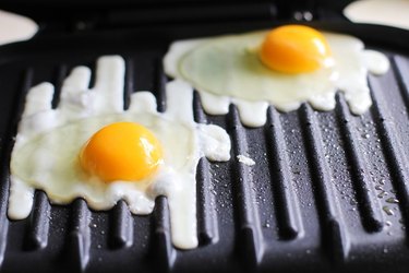Sunny-side-up eggs cooking on a George Foreman Grill.