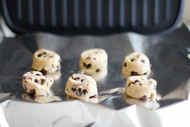 Cookie dough balls on a grill covered with foil.