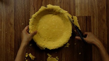 Trimming excess gluten-free, low-carb coconut flour rolled pie crust dough in pie pan.