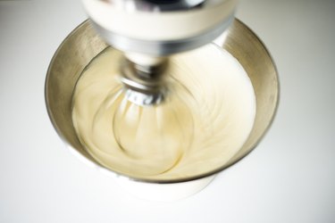Electric  beater whisking cream and sugar in a metal mixing bowl.