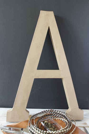 Paper mache letter "A" with a roll of nailhead trim in front.