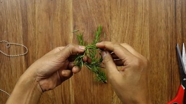 Bending rosemary sprig to create a mini Christmas wreath for DIY gift tag.