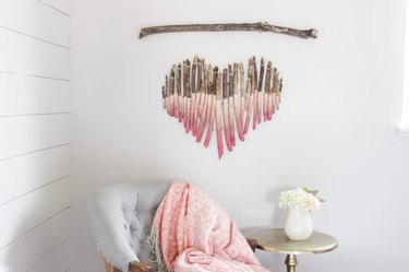 A wooden wall hanging in the shape of a heart hanging over a chair and table