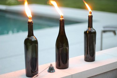 Three wine bottle tiki torches lined along a pool