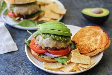 Cheeseburger with lettuce, tomato, onion, pesto sauce, and avocado