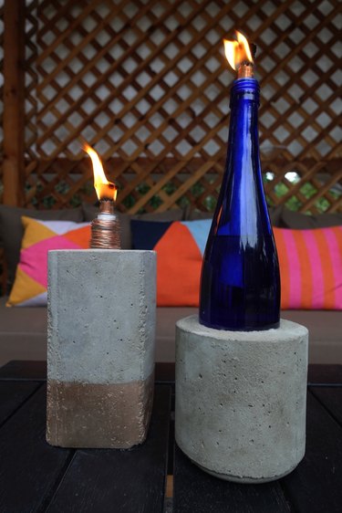 DIY concrete tabletop tiki torches out of used glass bottles on outdoor coffee table.