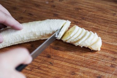 Knife slicing a whole peeled banana.