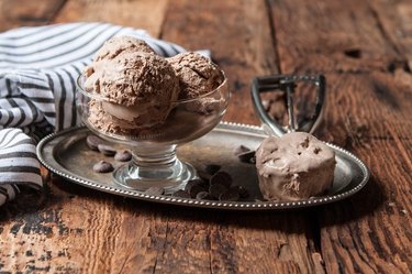 A bowl of chocolate ice cream on a silver platter with an ice cream scoop