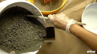 Pouring concrete into mold for DIY concrete tabletop tiki torches out of used glass bottles.
