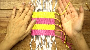 Weaving in loose yarn tails for DIY coasters on a cardboard loom.