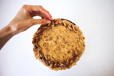 Hand placing pecans around the top of the cake.