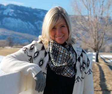 A blonde woman smiling at the camera wearing a white patterned cardigan outside