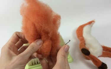 Hands holding a bunch of wool roving with a fox body in the background