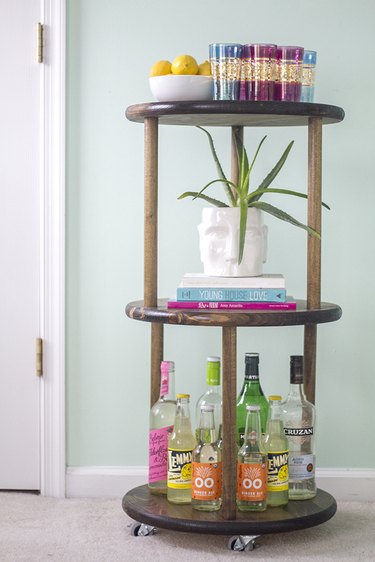 Fill the three tiers of the wooden cart with bar accessories and bottles.