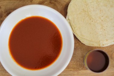 Bowl of enchilada sauce next to a stack of flour tortillas.