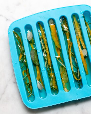 Ice cube molds packed with fresh herbs, citrus peels and water, ready for freezing