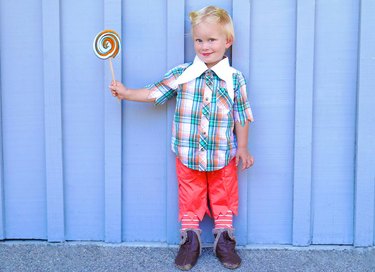 A toddler in a Munchkin costume holding a big lollipop.