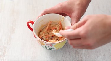 stirring carrots and walnuts into mug cake batter