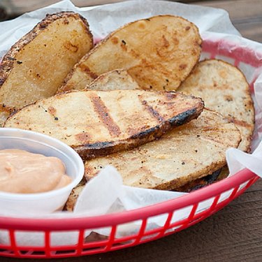 Grilled potatoes in a basket with dipping sauce.