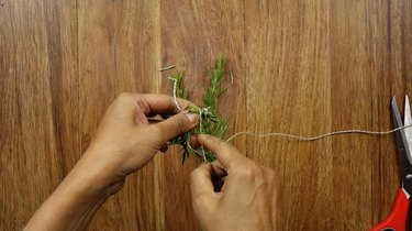 Wrapping rosemary sprig to create a mini Christmas wreath for DIY gift tag.