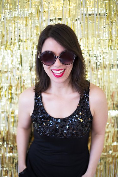 Woman in black dress and sunglasses in front of a gold backdrop