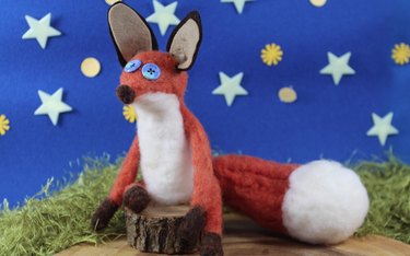 Orange wool felted fox in front of a starry background.