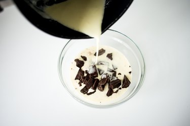 Pouring hot cream over chocolate pieces in a glass bowl.