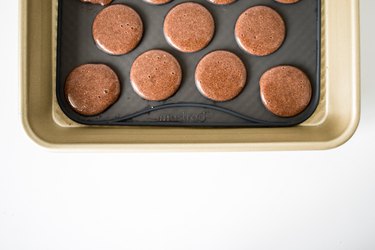 Macaron batter circles sitting on a baking tray.
