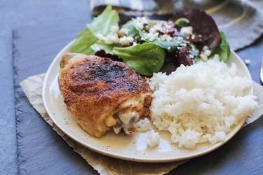 Baked chicken thigh on a plate with rice and salad