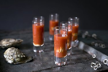 Six bloody mary oyster shooters on a metal tray