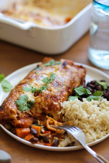 Plate with two vegetarian enchiladas, black beans and rice.
