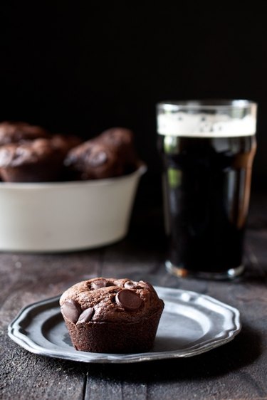 A chocolate stout chocolate chip muffin on a plate next to a pint of chocolate stout.