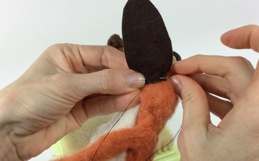 Female hands sewing a brown oval of felt to an orange fox body.