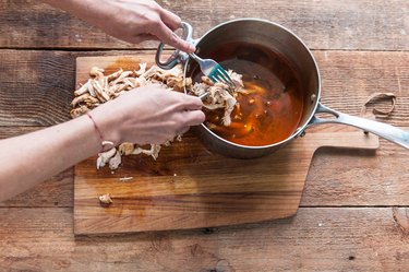 Shredding chicken over pot of broth