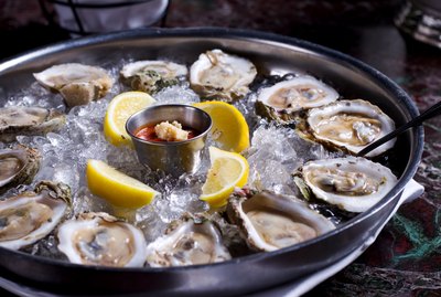 Fresh raw oysters with lemons on ice in metal tray