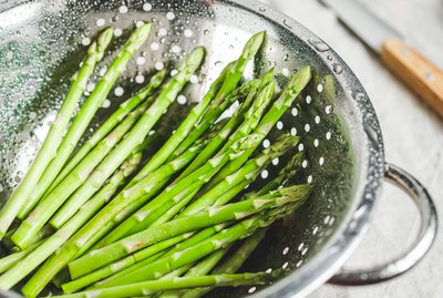 Washed asparagus in a metal colander on a kitchen table. Preparation vegetarian healthy food.