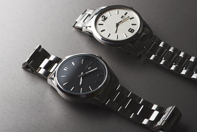 Two metallic wristwatches on gray background. Horizontal studio shot.