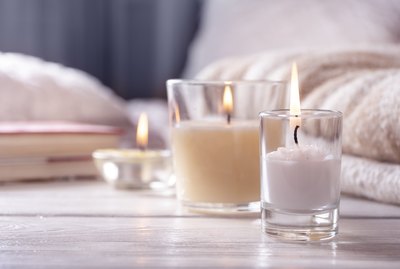 Home interior. Still life with detailes. Several candles on white wooden table in front of bed, the concept of cosiness.