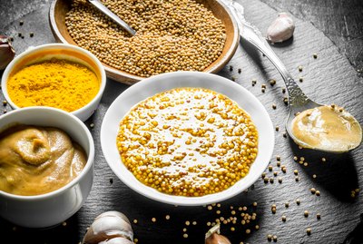 Assortment of different types of mustard on a stone Board.