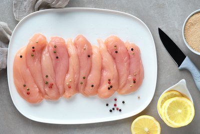 Raw chicken fillet. Meat with breadcrumbs, herbs , lemon and cooking oil. Top view on light colored stone