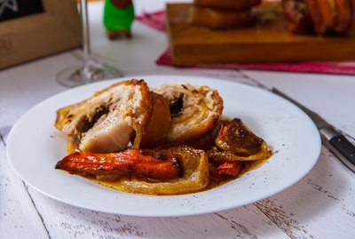 Sliced pork roll with vegetables on a white plate side view. Porketta