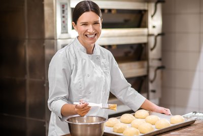 Smiling woman in uniform preparing buns for baking