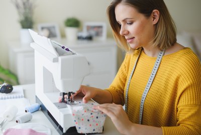 Young woman sewing protective face mask indoors at home, quarantine concept.