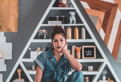 Woman in coveralls sits on table in front of wooden shelf