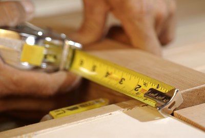Close-up of man's hands as he measures a piece of wood.