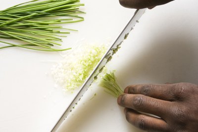 African-American male hands using large kitchen knife to chop fresh chives.