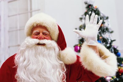 Father Christmas standing with arms up, smiling, portrait, Christmas tree in background