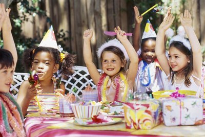 Group of children sitting at a table at a birthday party with their arms raised