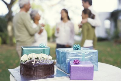 Gifts and birthday cake on table, close up, family in background