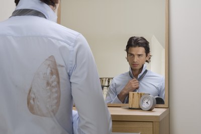 Young man adjusting tie in mirror, iron stain on shirt, rear view